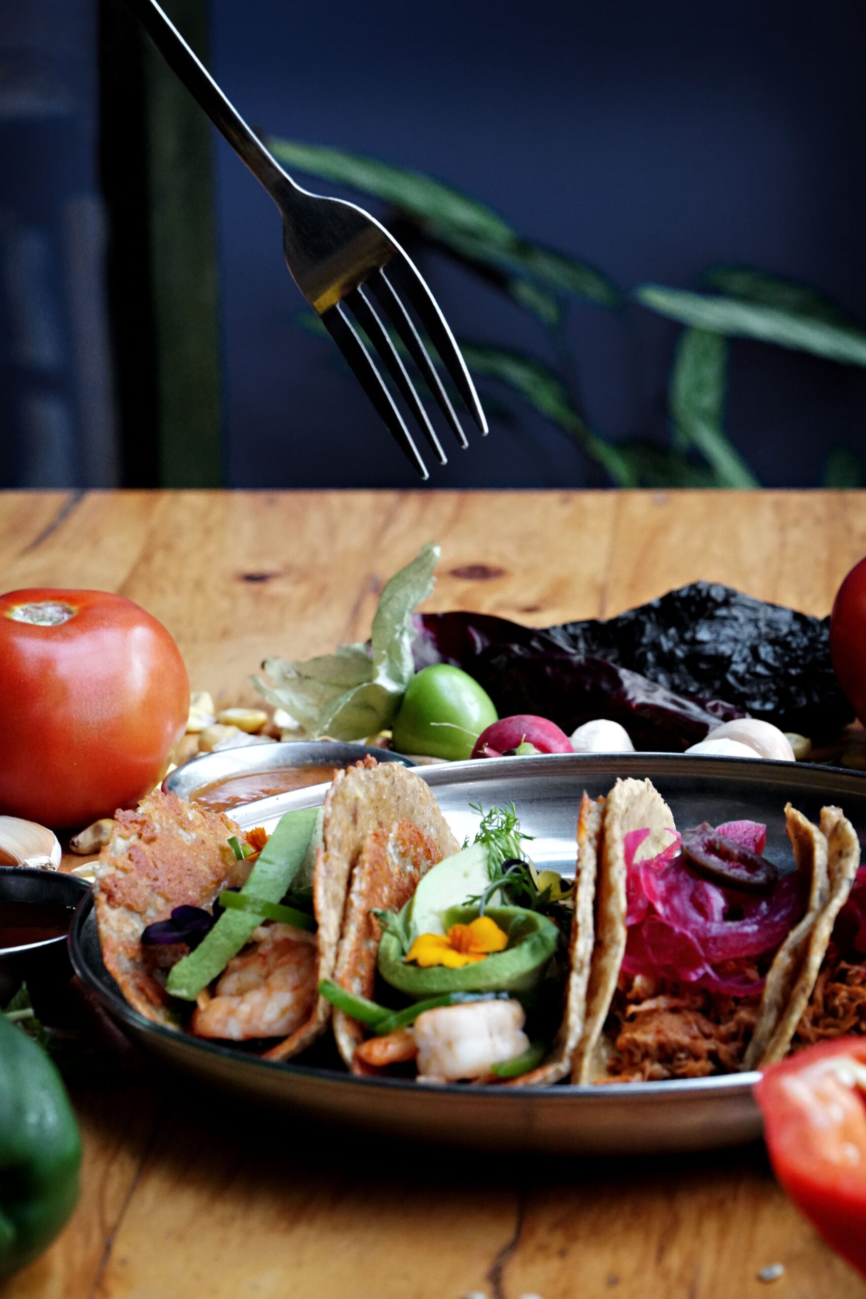 Close-up of assorted Mexican tacos with fresh vegetables, herbs, and vibrant garnishes on a wooden table.