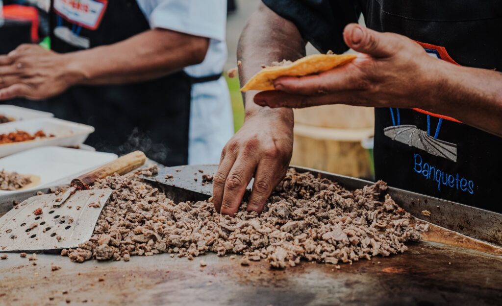 Close-up of a vendor preparing delicious tacos on a hot griddle at an outdoor street food market.
