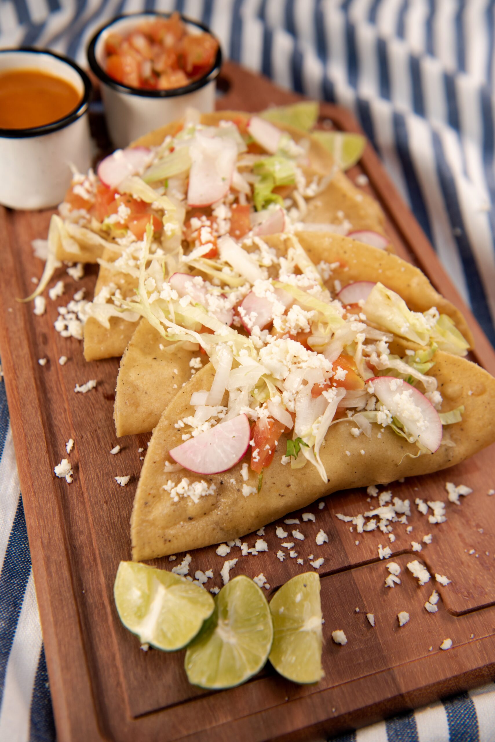 Close-up of Mexican street tacos topped with radish, lettuce, and cheese on a wooden board.